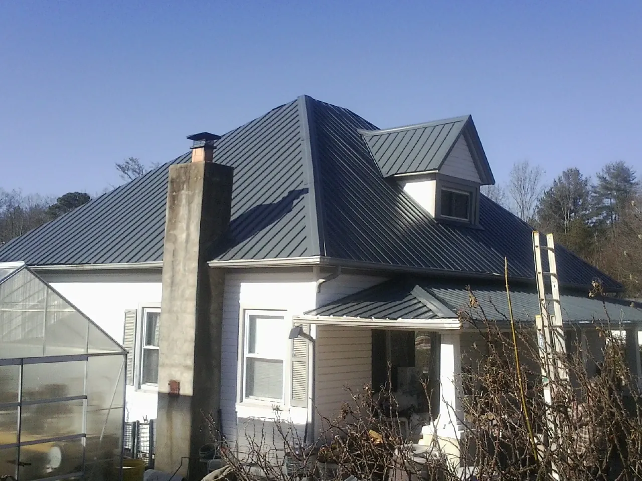 Dark blue standing seam metal roof on a white farmhouse with dormer — Slate & Tile Roof Repair by Roofing Brothers in Galion