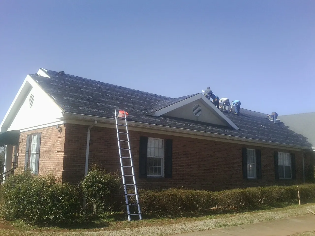 Crew tearing shingles off a brick ranch roof with a ladder set — Emergency Roof Repair work by our crew in Galion
