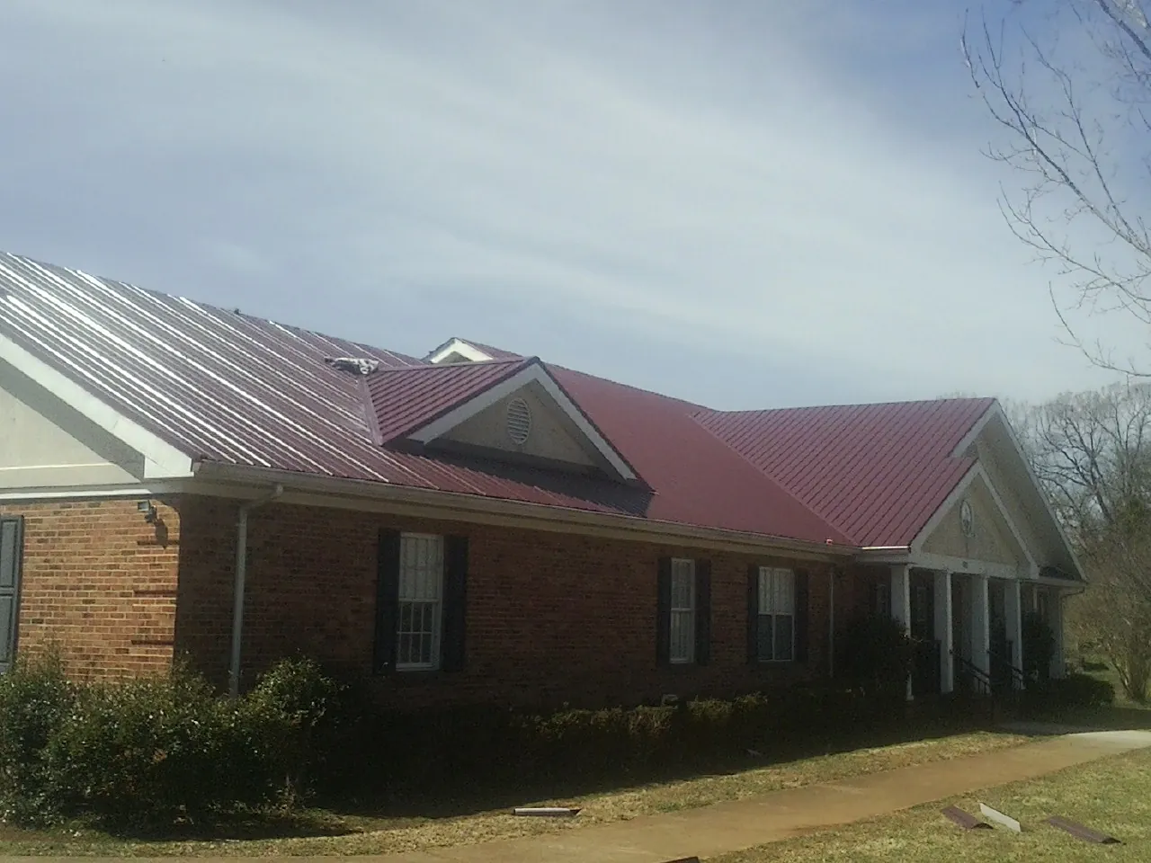 Red metal roof with gabled entries on a long brick building, from a Hail Damage Roof Repair job in Galion