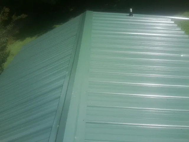 New green metal panels meeting at the ridge of a roof — Flat Roof Repair work by our crew in Galion