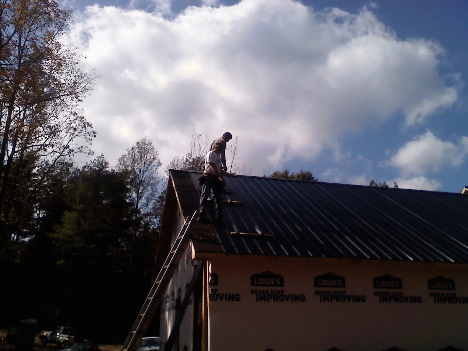 Roofer fastening dark metal panels high against a cloudy sky, from a Roof Inspection job in Galion