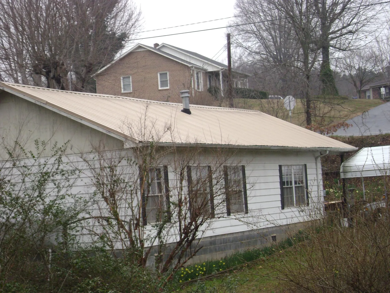 Tan metal roof on a white sided house set into a hillside — Commercial Roofing by Roofing Brothers in Galion